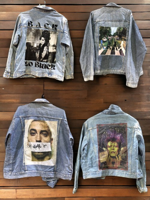 a group of rock band printed denim jackets hanging on a wooden wall